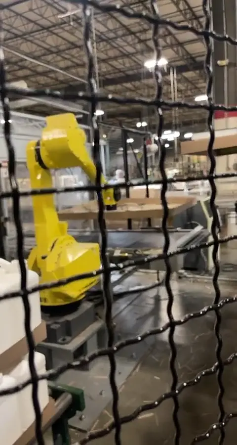 Robotic palletizing arm working behind wire-mesh machine guarding