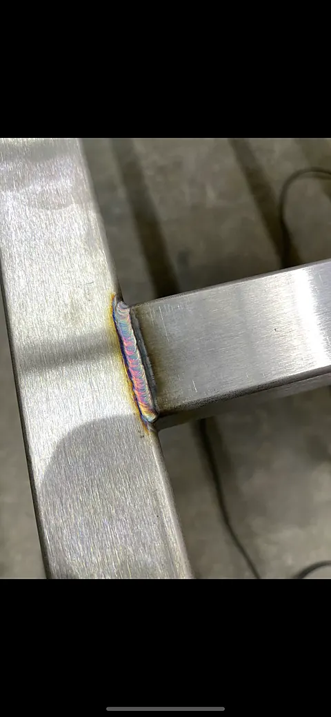 Close-up of a TIG fillet weld with rainbow heat tint joining stainless square tubing