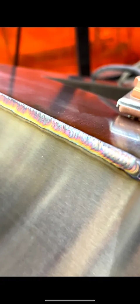 Stacked TIG weld bead with iridescent coloring running along a stainless panel edge