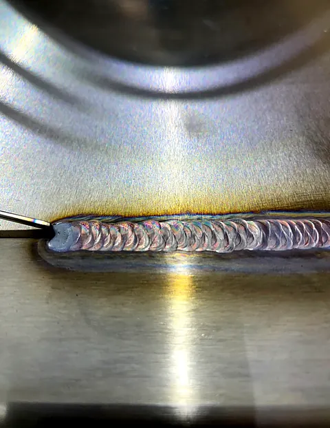 Uniform stack-of-dimes TIG weld bead across a brushed stainless steel plate