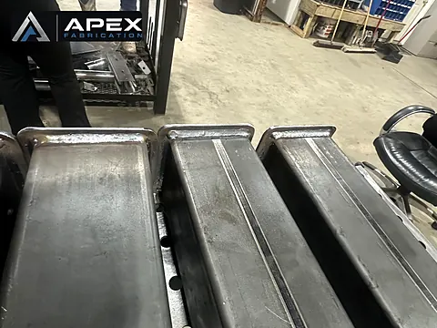 Three welded steel channel assemblies lined up on the shop floor