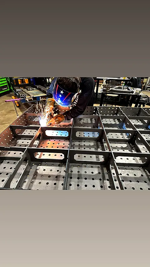 Welder in a flag-design helmet MIG welding a perforated steel fabrication as sparks fly