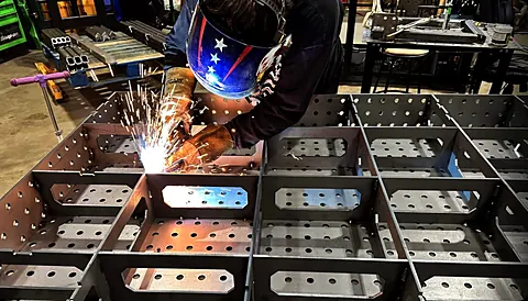 Welder joining perforated steel compartments with bright sparks in the fabrication shop