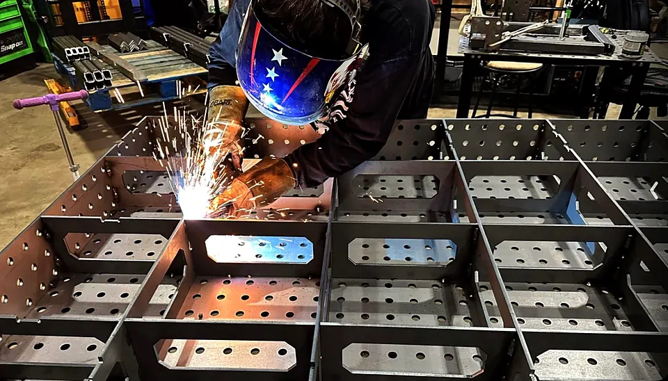 Welder joining perforated steel compartments with bright sparks in the fabrication shop