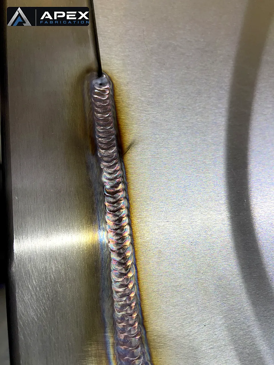 Uniform TIG weld bead with copper and blue heat tint joining brushed stainless steel plates
