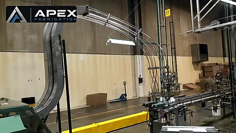 Curved overhead air conveyor arching across a bottling plant aisle toward a packaging line