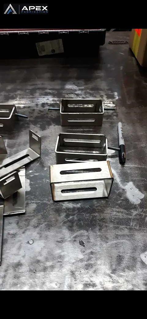 Small formed stainless steel brackets with slotted faces arranged on a welding table
