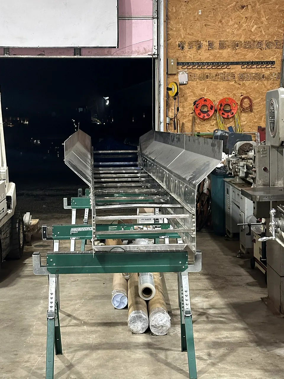 Long stainless steel trough conveyor section supported on stands inside the fabrication shop