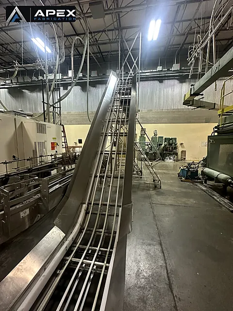 Stainless steel incline conveyor carrying product up from a bottling line in a plant