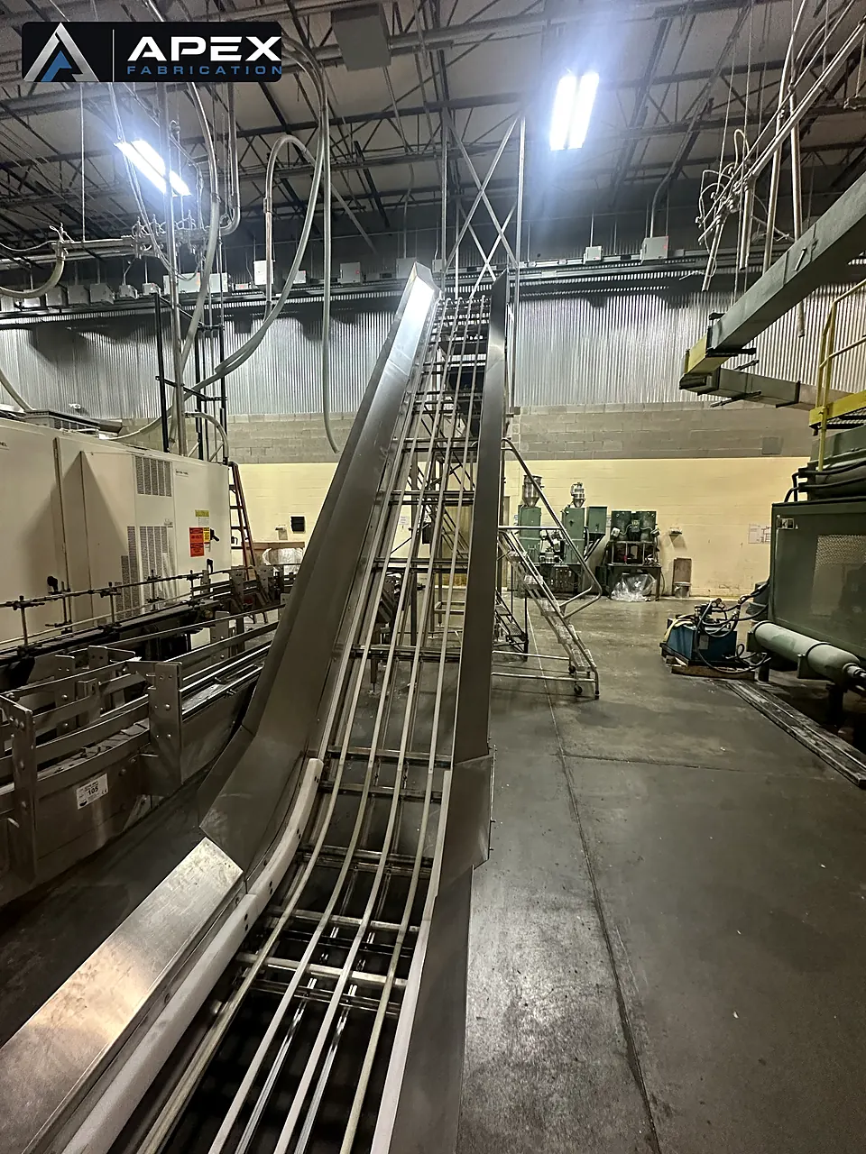Stainless steel incline conveyor carrying product up from a bottling line in a plant