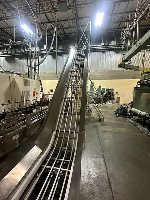 Tall stainless incline conveyor rising from the filling line inside a production plant