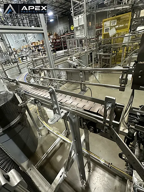Tabletop chain conveyor with stainless guide rails running through an industrial production floor
