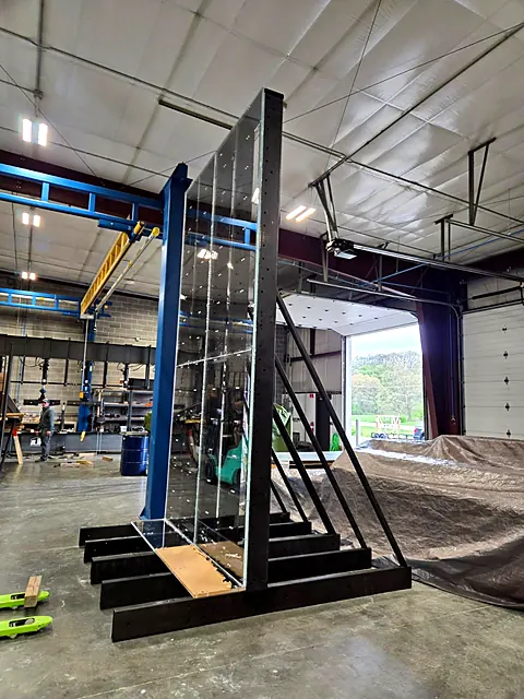 Custom-fabricated black steel A-frame rack holding a clear panel in a fabrication shop