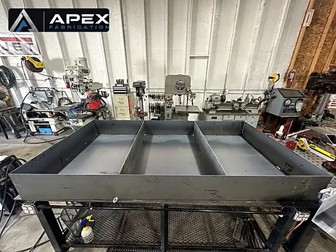 Large welded steel containment pan with divider walls on a stand in the fabrication shop
