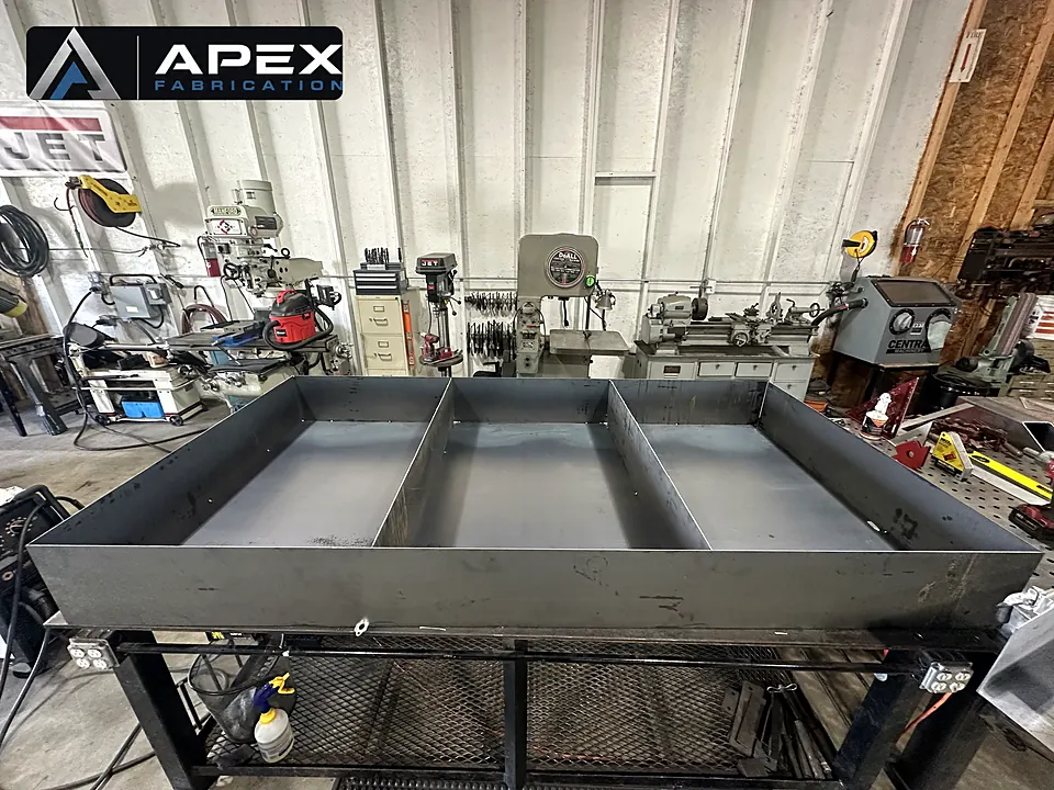 Large welded steel containment pan with divider walls on a stand in the fabrication shop