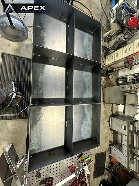 Divided steel containment tray with tab-and-slot welded joints on a shop table
