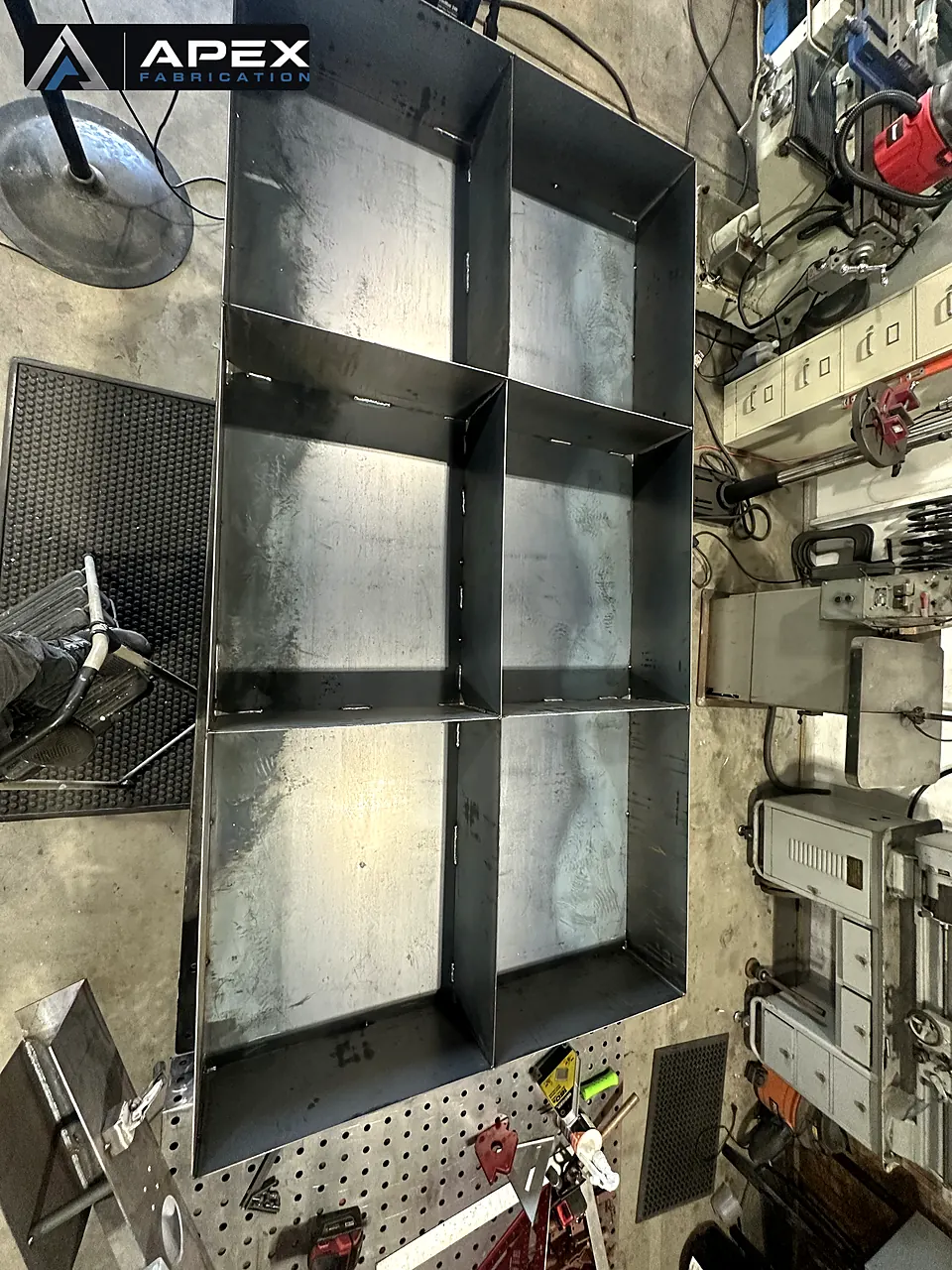 Divided steel containment tray with tab-and-slot welded joints on a shop table