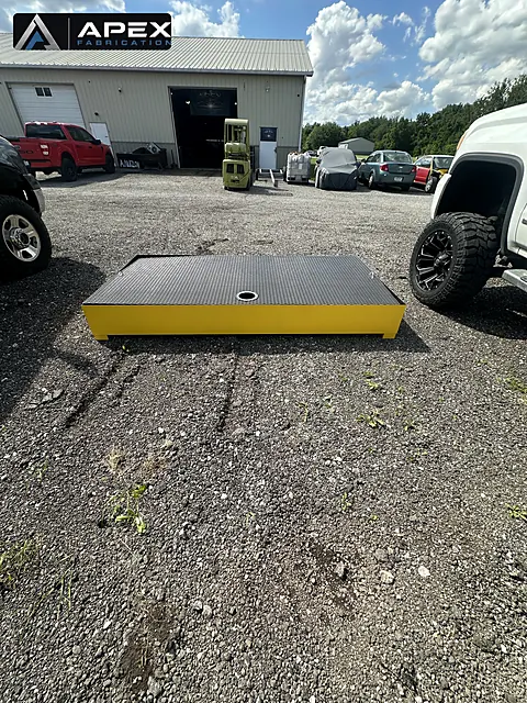 Yellow powder-coated spill containment platform with black grating top in the yard