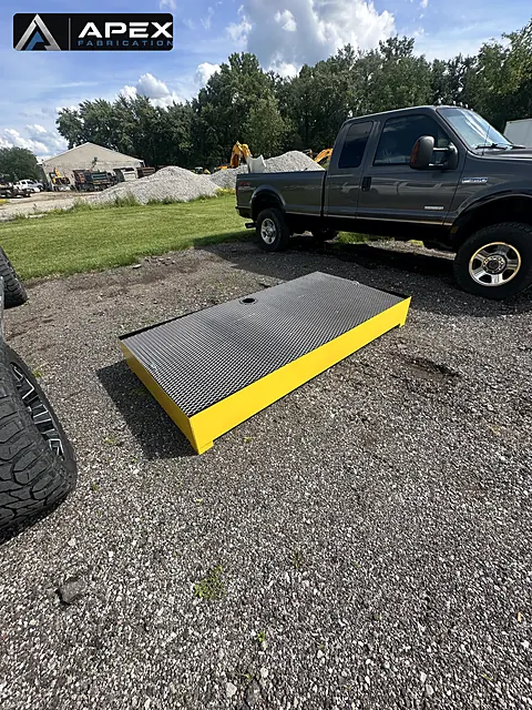Completed yellow spill containment platform with grating deck staged in the gravel yard