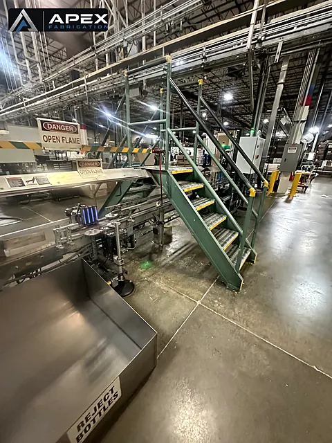 Steel crossover stairway installed over a bottling line conveyor in an industrial plant