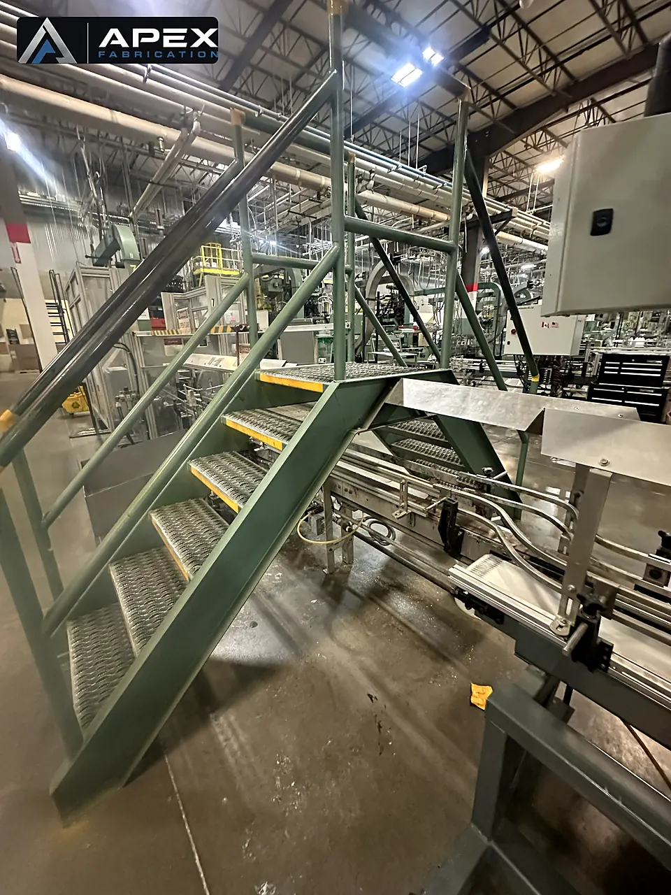 Fabricated steel crossover stairs with tread plating installed above a plant conveyor