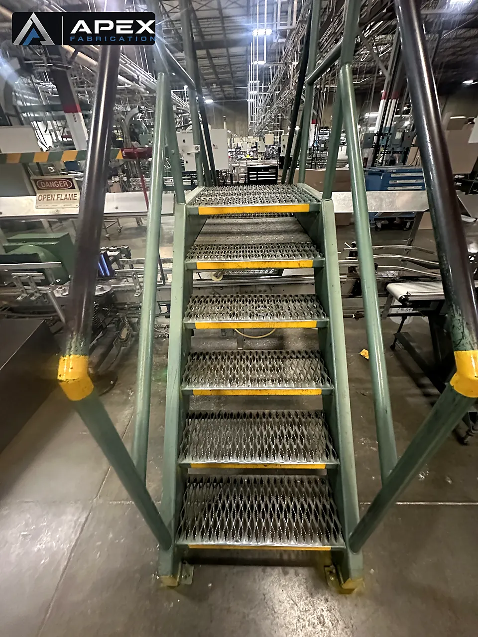 Head-on view of steel crossover stairs with perforated treads inside a production facility
