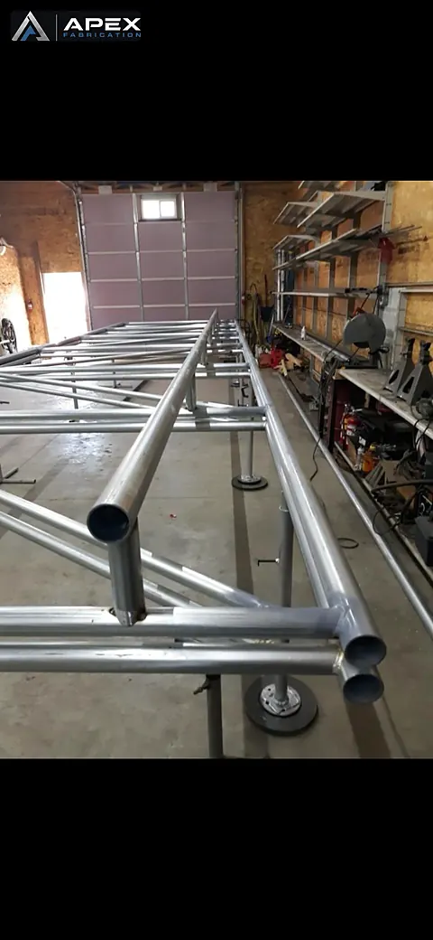 Close view of welded round-tube truss joints and base flanges in a fabrication shop