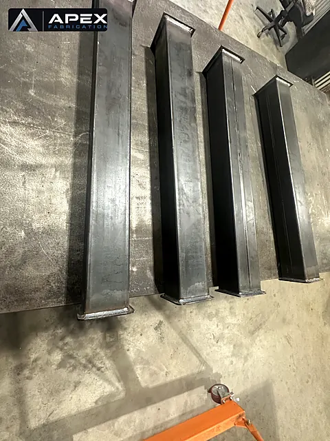 Four welded steel columns with base plates laid out side by side in the shop